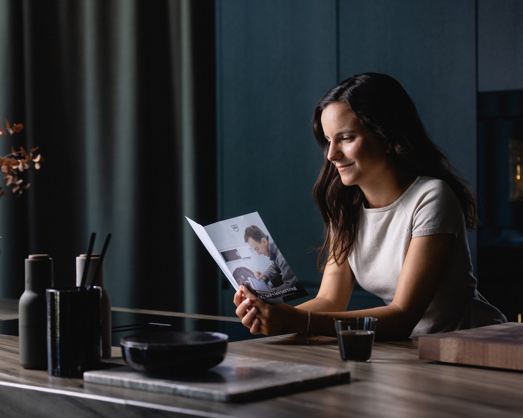 Modern kitchen with dark elements and stylish accessories, person reads brochure.