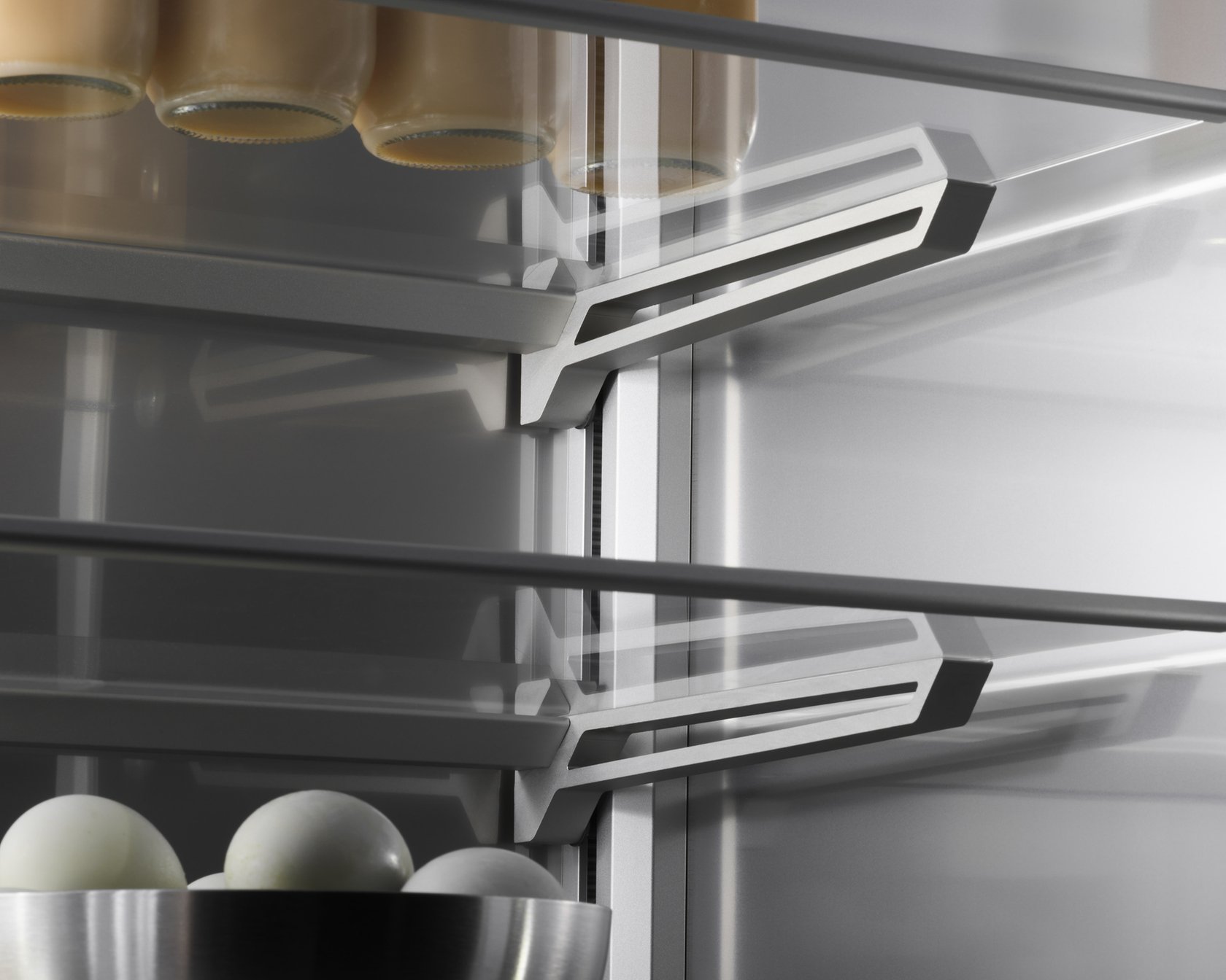 Modern refrigerator interior with milk bottles and a bowl of eggs on glass shelves.
